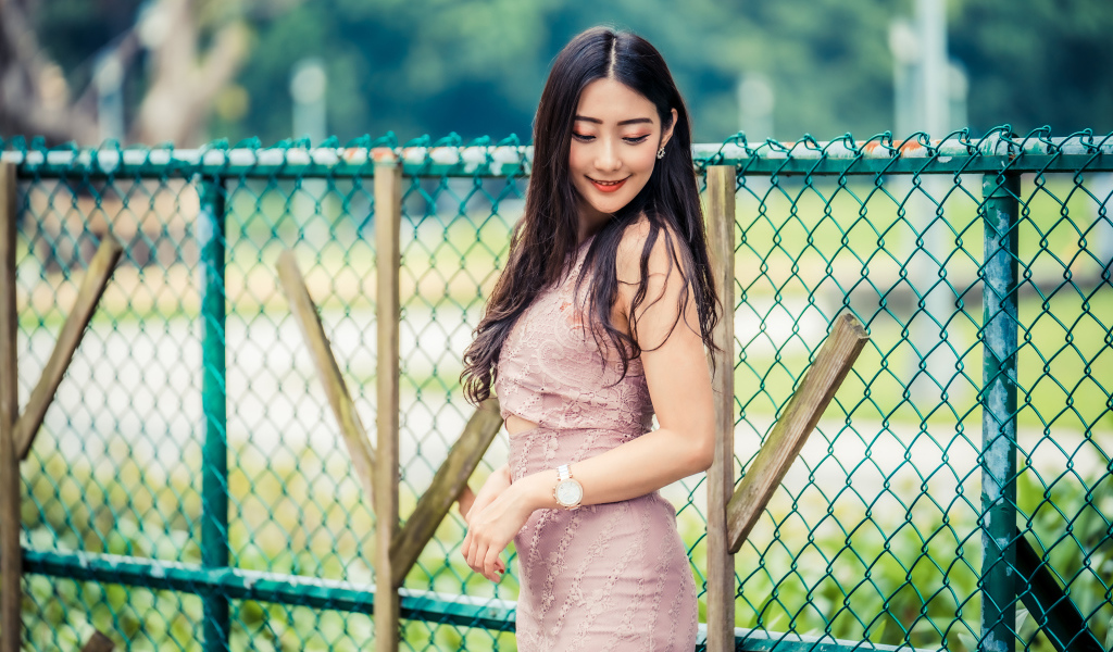 Милая азиатка в платье стоит под забором