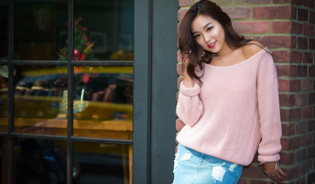 Cute Asian woman in pink sweater stands against the wall