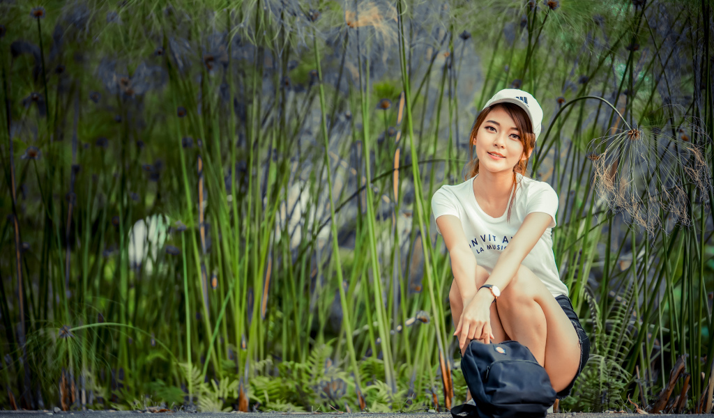 Милая девушка в кепке сидит на дороге с рюкзаком