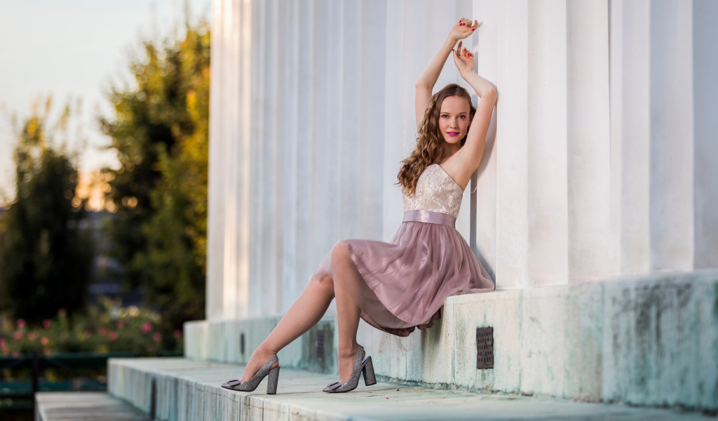 Милая девушка в юбке сидит на ступеньках у здания 