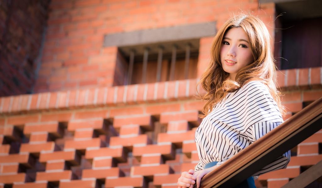 Милая девушка в полосатой рубашке стоит на ступеньках 