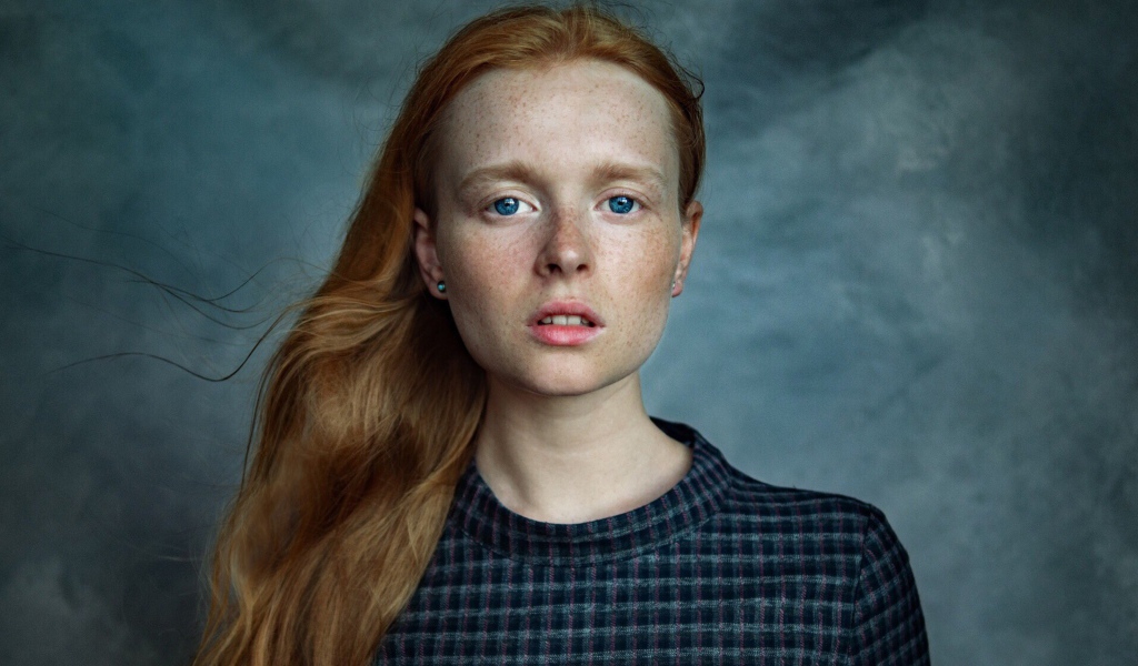 Милая рыжеволосая голубоглазая девушка с веснушками на лице на сером фоне