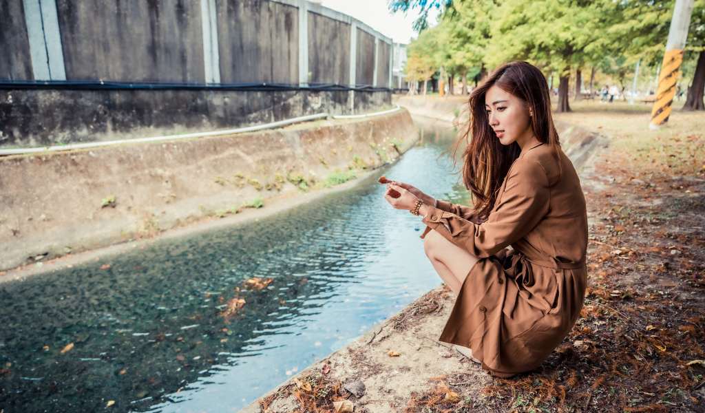 Мечтательная девушка азиатка сидит у воды