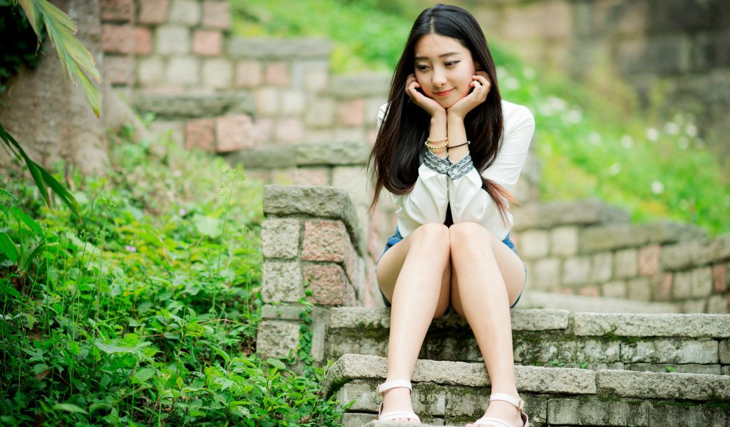 Мечтательная девушка азиатка сидит на ступеньках 