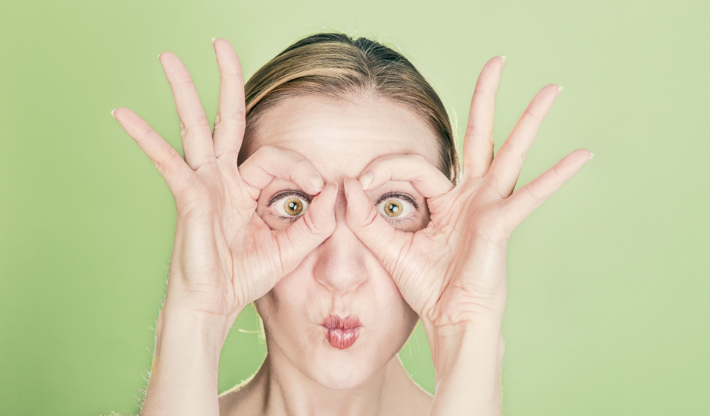 Смешная девушка делает руками очки на лице