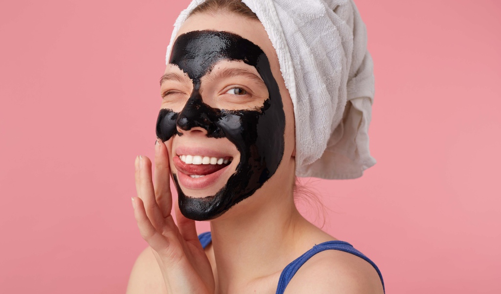 Смешная молодая девушка с черной косметической маской на лице 