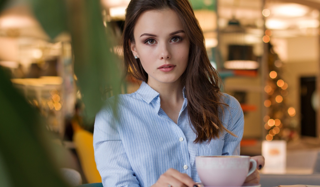 Девушка в голубой рубашке с чашкой кофе на столе в кафе