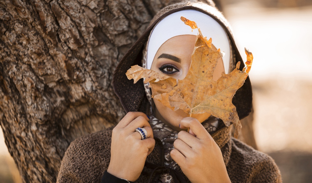 Девушка в пальто с закрывает лицо листом