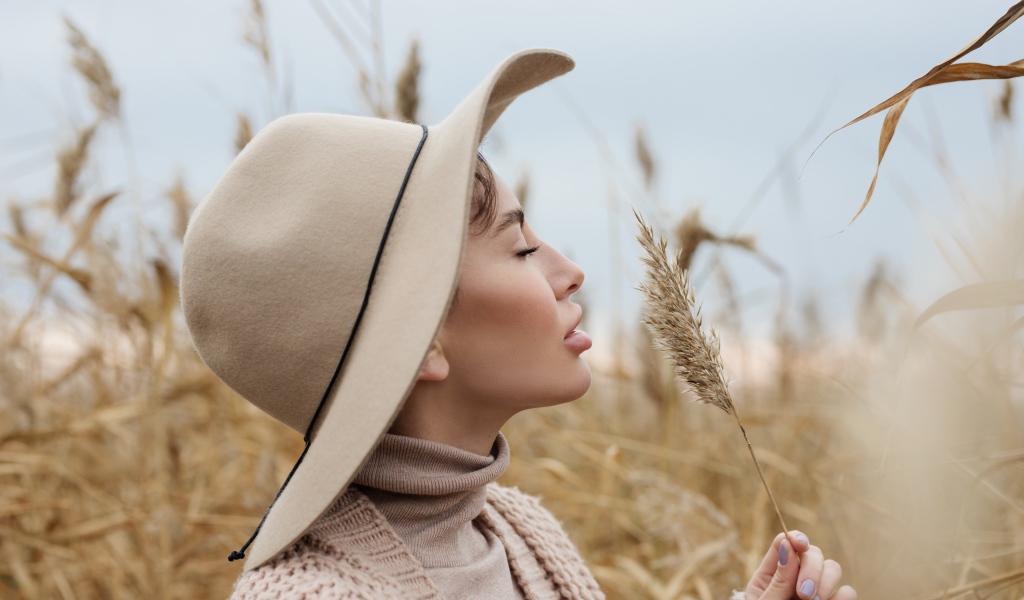 Девушка в шляпе с закрытыми глазами держит колосок 