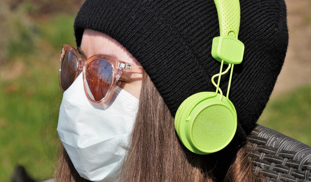 Девушка в медицинской маске на лице, в черной маске и наушниках