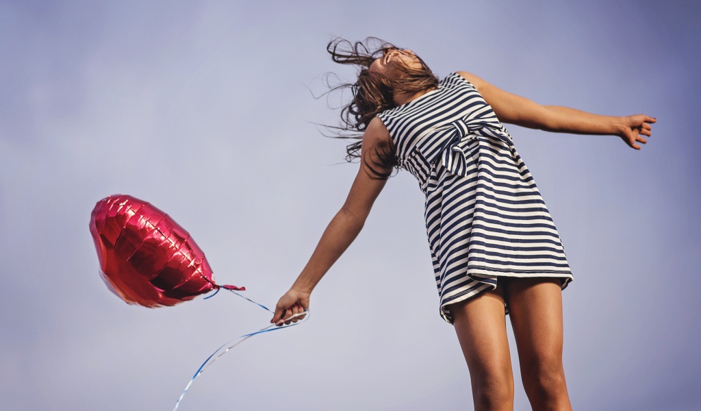 Девушка в полосатом платье прыгает с шариком 