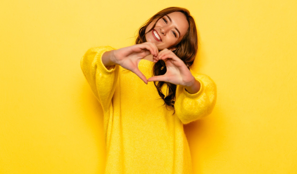 Девушка в желтом свитере показывает сердце руками