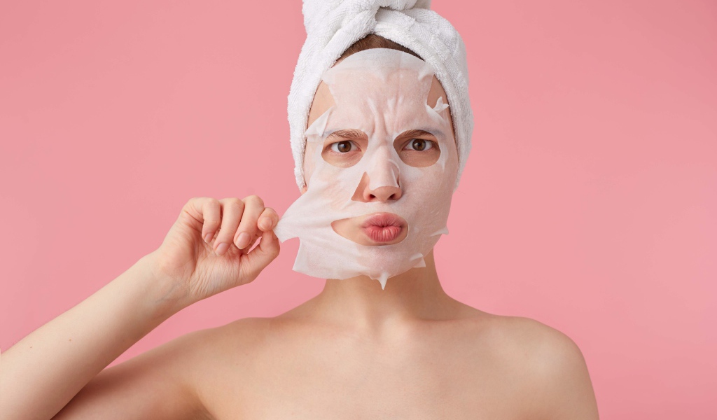 Девушка снимает косметическую маску с лица на розовом фоне 