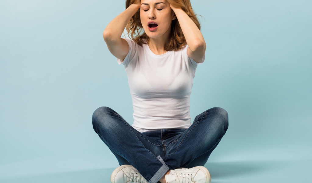 Девушка с руками в волосах сидит в джинсах на голубом фоне