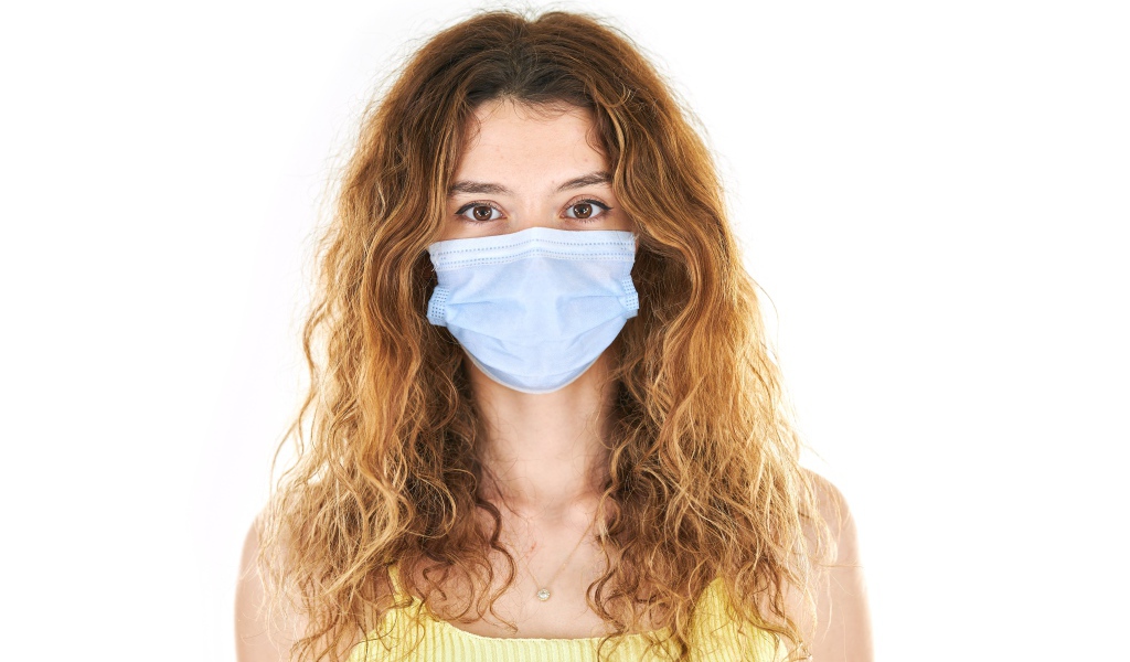 Длинноволосая девушка в маске от коронавируса на белом фоне