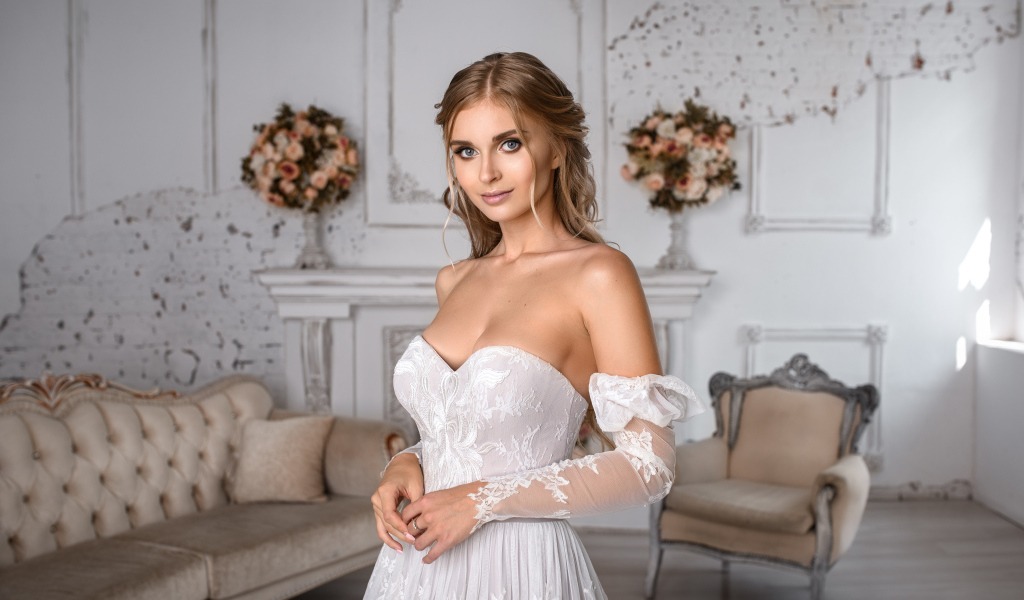 Милая девушка в свадебном платье в комнате с диваном