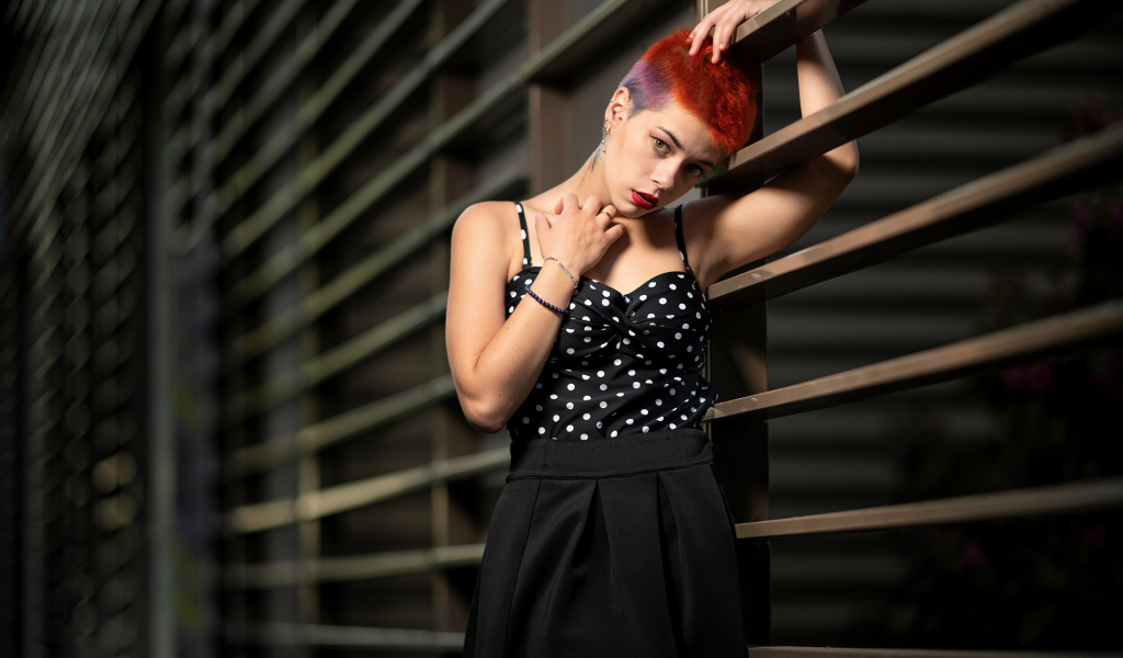 Эпатажная девушка с короткой стрижкой стоит у забора 