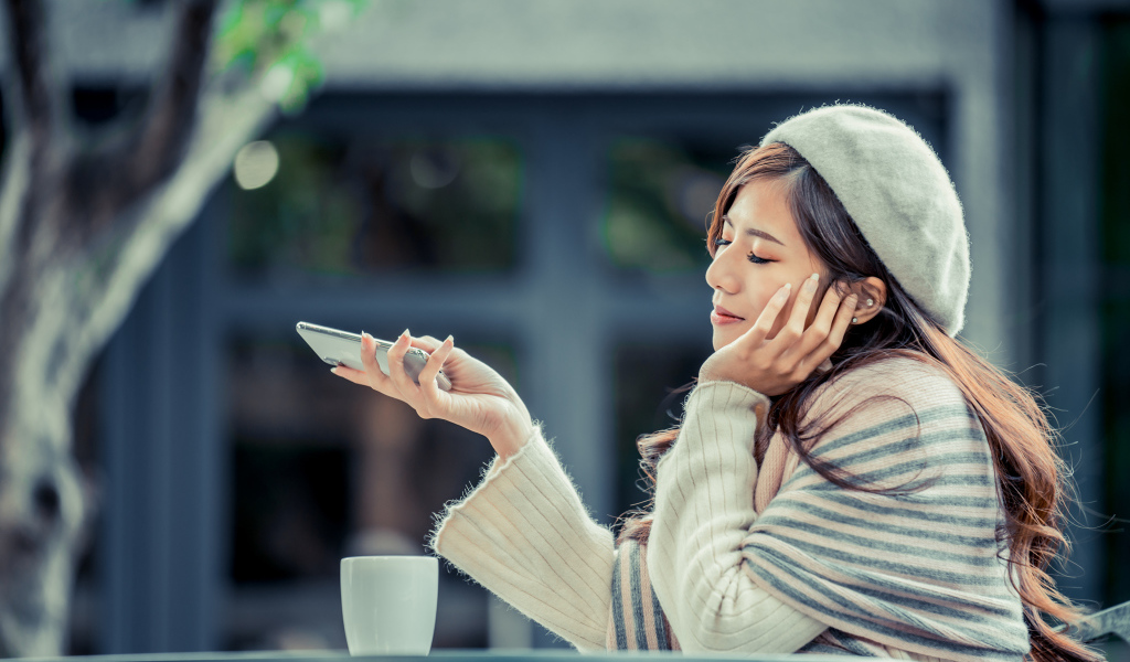 Мечтательная девушка с телефоном сидит в кафе 