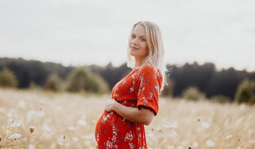 Беременная девушка в красном платье на поле