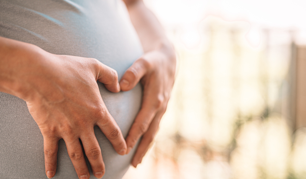 Беременная женщина держит руки на животе 