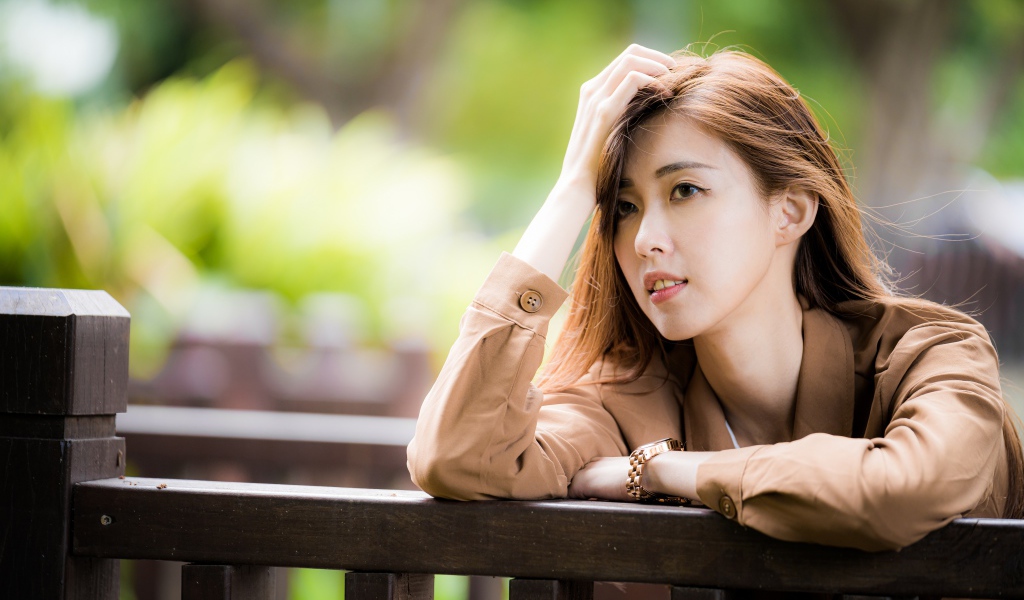 Грустная девушка азиатка стоит у деревянных перил 