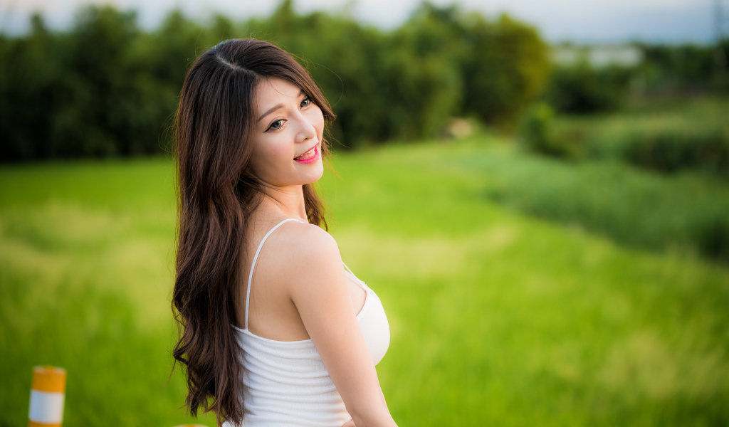 Улыбающаяся девушка азиатка на фоне зеленой травы