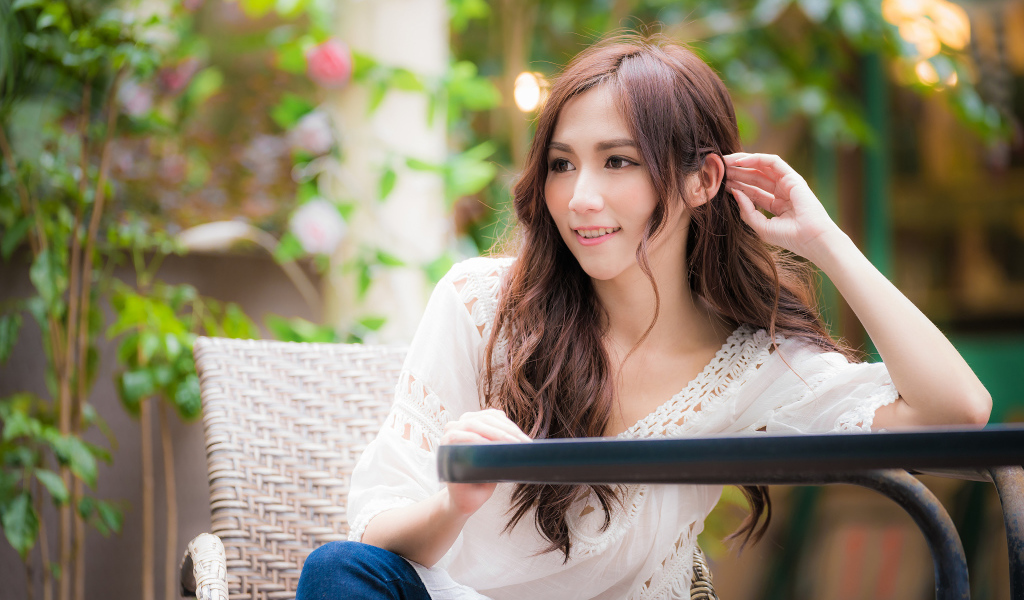 Улыбающаяся девушка азиатка сидит за столом в кафе