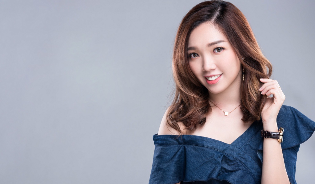 Улыбающаяся девушка азиатка с часами на руке на сером фоне