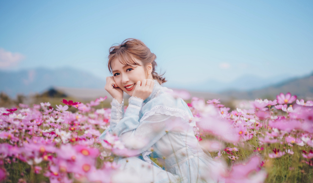 Улыбающаяся девушка азиатка на поле с цветами космеи 