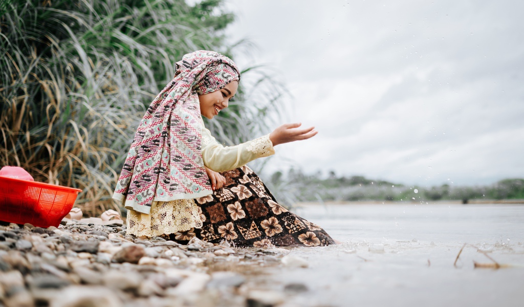 Улыбающаяся девушка азиатка сидит у воды