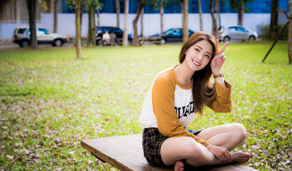 Улыбающаяся девушка азиатка сидит на лавке в парке 