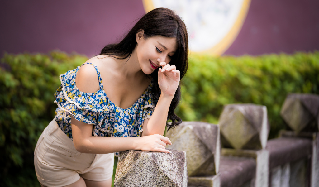 Улыбающаяся девушка азиатка стоит у каменных перил