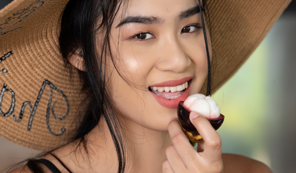 Улыбающаяся азиатка в шляпе с фруктом в руке