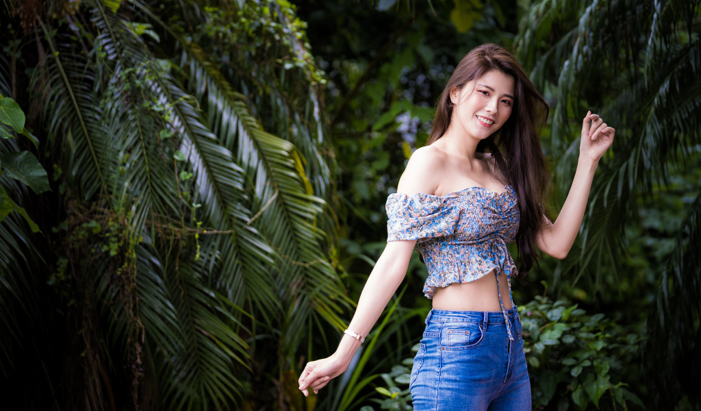 Улыбающаяся азиатка на фоне зеленых листьев