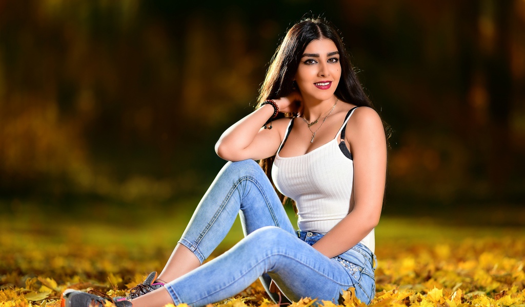 Улыбающаяся брюнетка сидит на опавшей листве