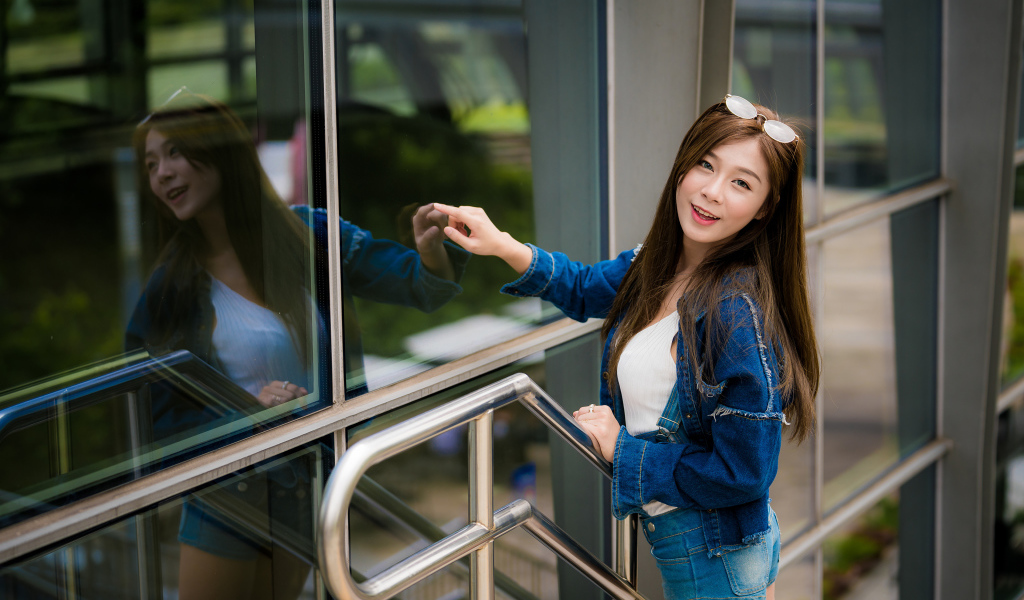 Улыбающаяся девушка в джинсовой куртке стоит у стены 