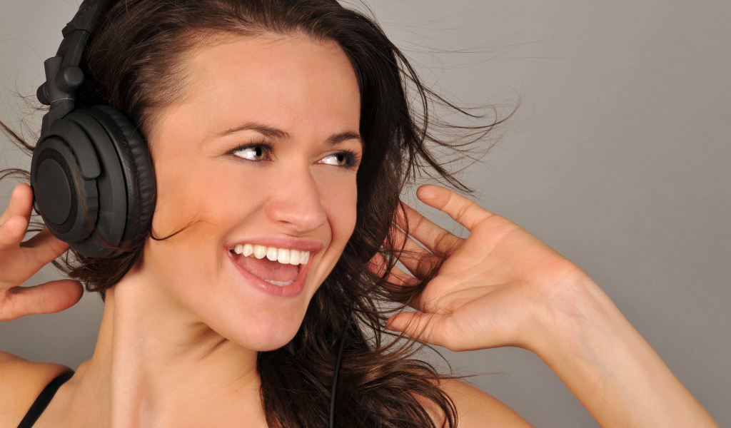 Улыбающаяся девушка в наушниках на сером фоне 