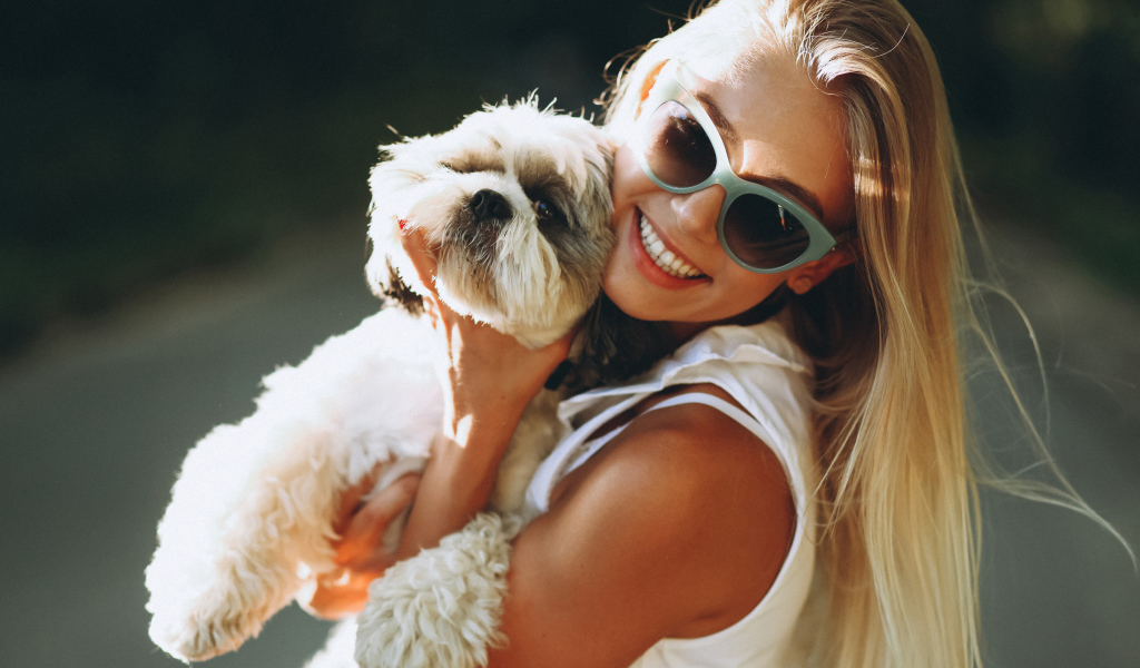 Улыбающаяся девушка в солнечных очках с собакой на руках