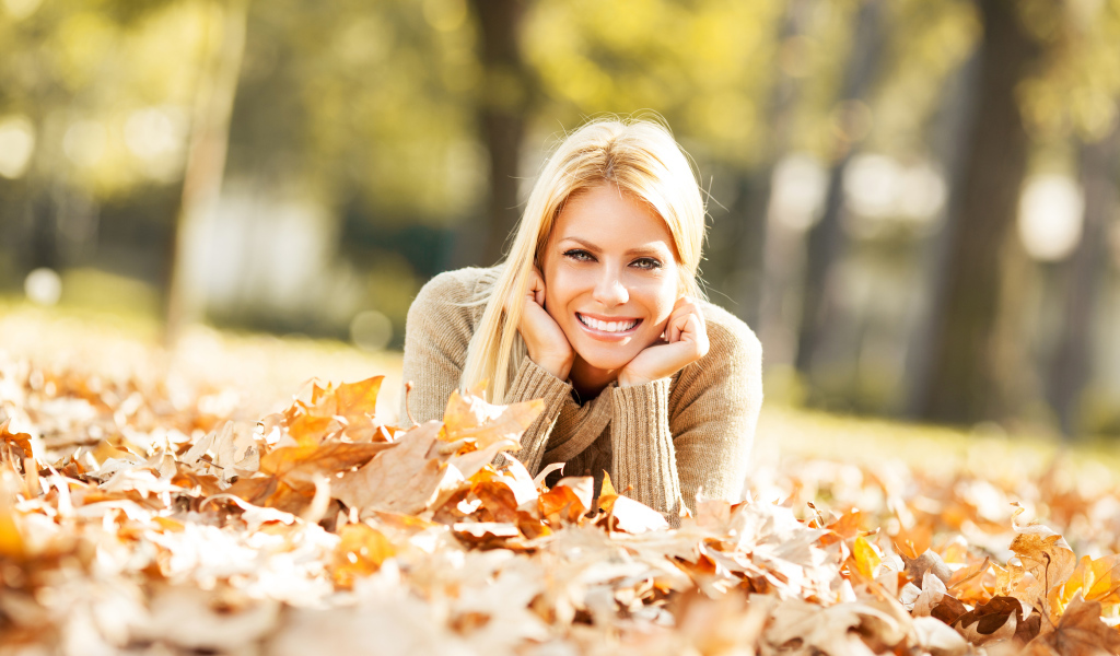 Улыбающаяся девушка лежит на сухой опавшей листве
