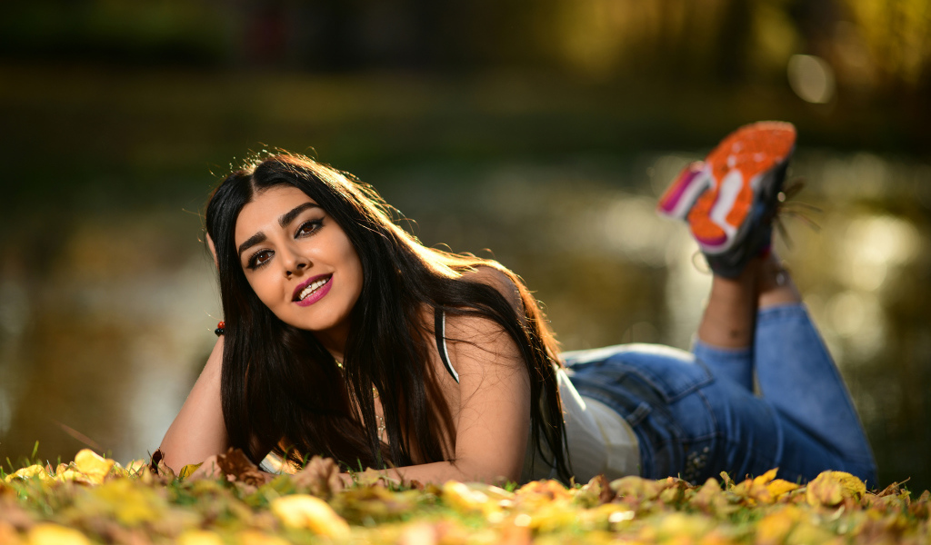 Smiling girl model lies on the ground with fallen leaves