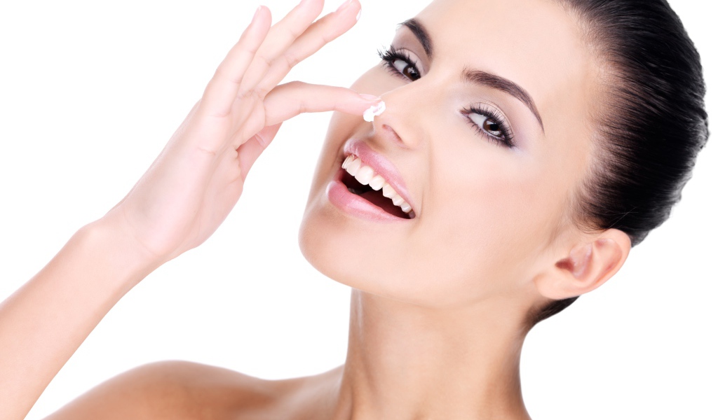 Улыбающаяся девушка мажет крем на нос 