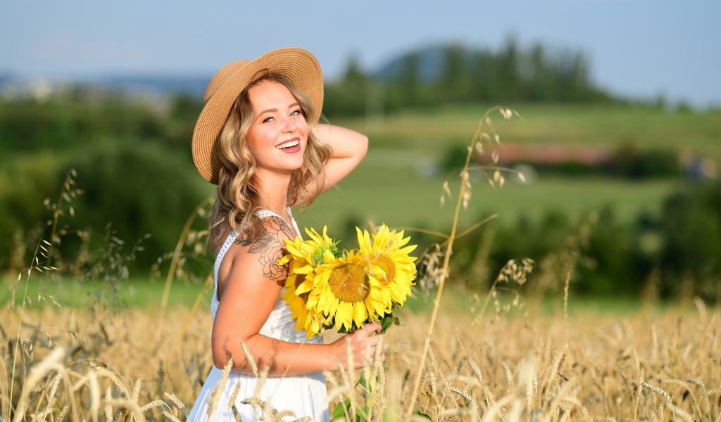 Улыбающаяся девушка с букетом подсолнухов на поле пшеницы
