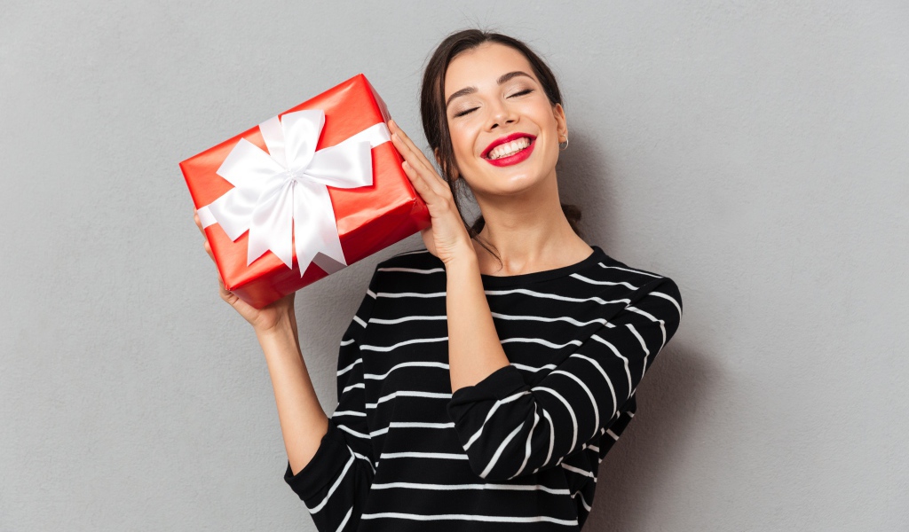 Улыбающаяся девушка с подарком в руках на сером фоне 