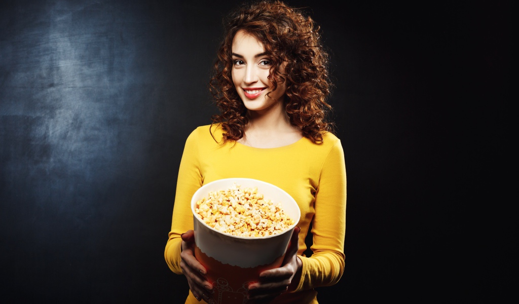 Улыбающаяся девушка с попкорном в руках на черном фоне 