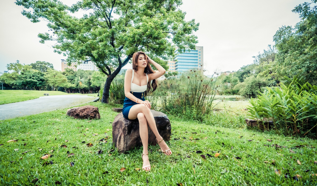 Эффектная девушка азиатка сидит на камне в парке