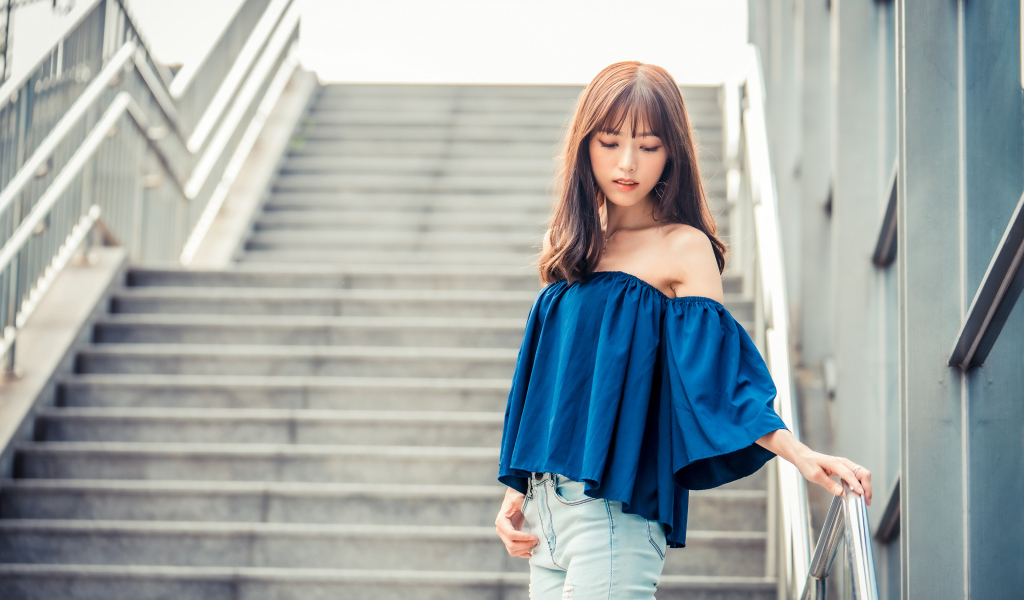 Стильная девушка азиатка с опущенной головой стоит на ступеньках 