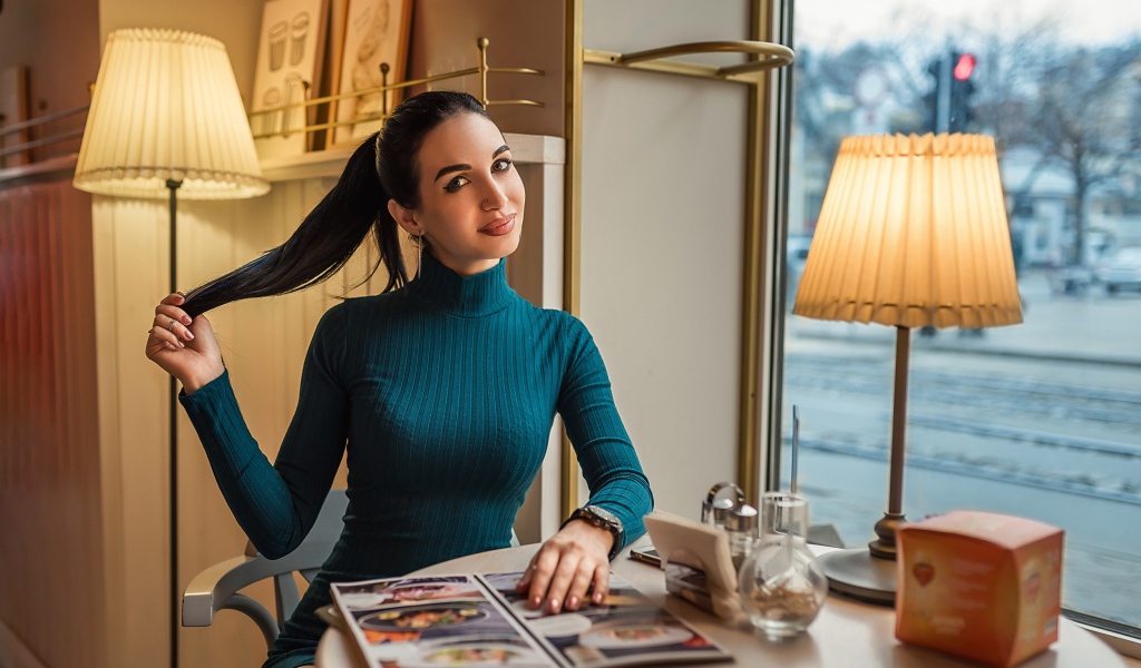 Стильная девушка в платье сидит в кафе у окна