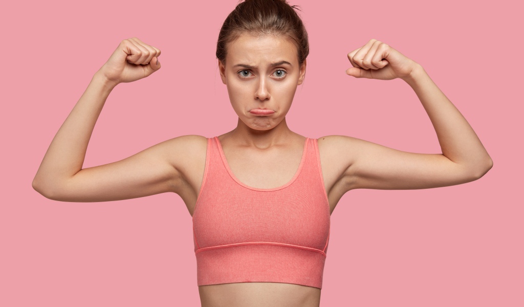 Расстроенная девушка без накаченных рук на розовом фоне