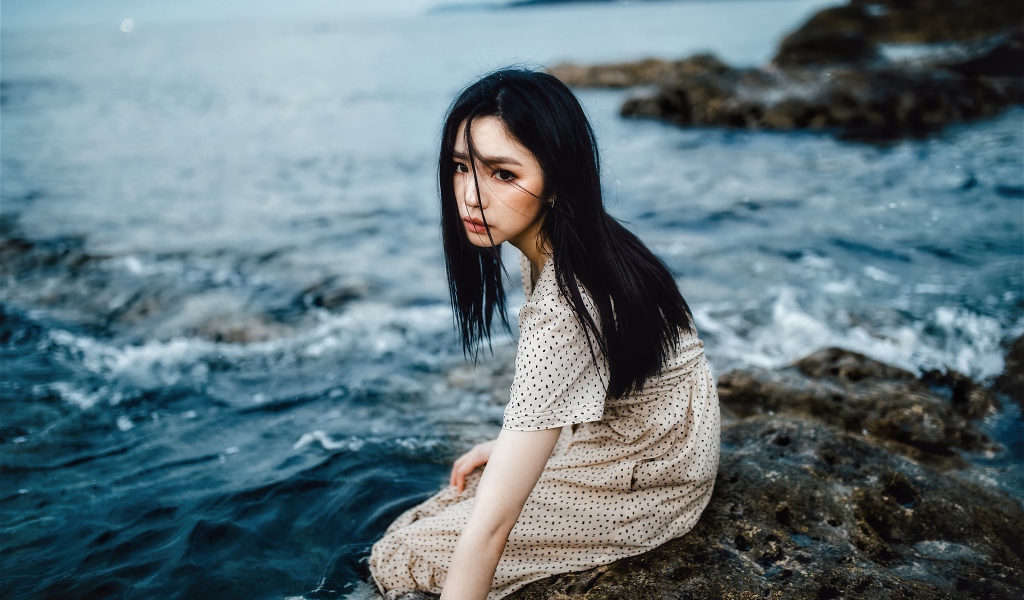 Young Asian girl sitting on a stone by the water