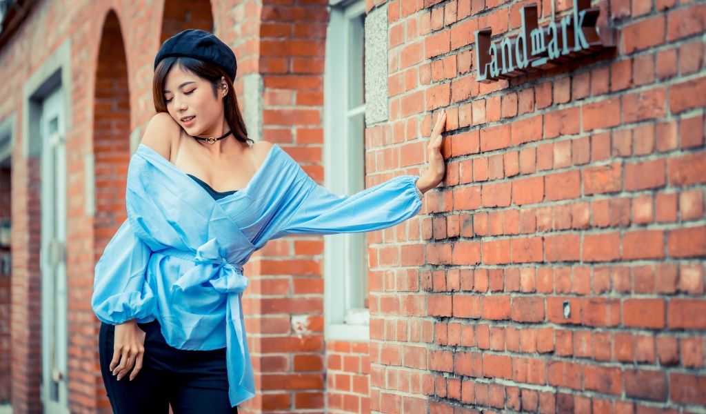 Молодая азиатка в черном берете стоит у стены 